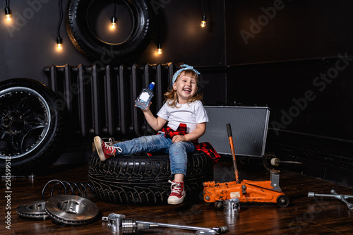 child laughs merrily in a car repair shop among tires and wheels holding a bottle of clean drinking water