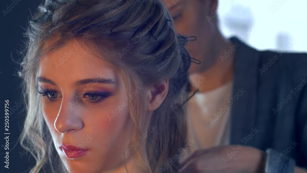 Makeup artist and hairdresser are preparing bride before wedding. Hairdresser-stylist with short stylish hairstyle applies makeup, makes false eyelashes, paints lips, curls girl, spectacular lighting