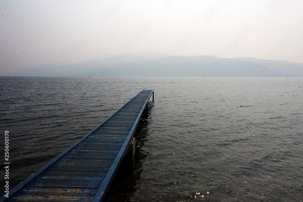 Pier, straight out to water, on a foggy cloudy day with background of mountain faraway.