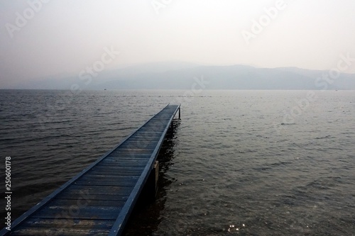 Pier, straight out to water, on a foggy cloudy day with background of mountain faraway.
