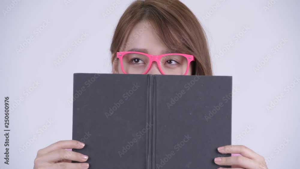 Face of young Asian nerd woman thinking while covering face with book