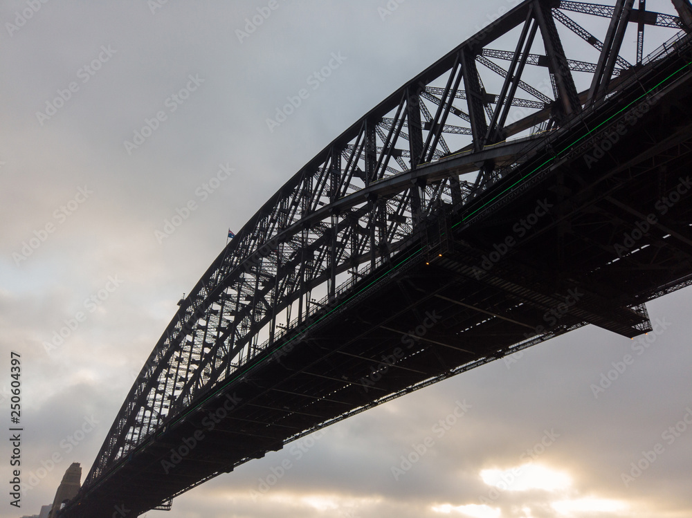 Obraz premium Sydney Harbour Bridge view from below with cloudy sky.