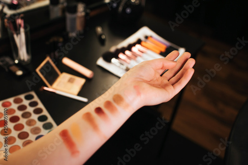 Woman's hands with eyeshadow examples on skin. Colorful palette. Brushes blush and mirror on table. Cut view. Close up.