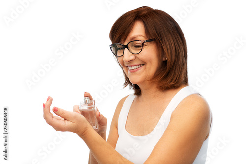perfumery, beauty and luxury concept - happy smiling senior woman spraying perfume to her wrist over white background