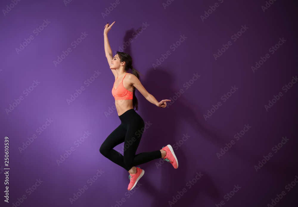 Sporty young woman jumping against color background