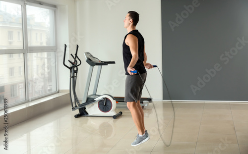 Sporty young man jumping rope in gym