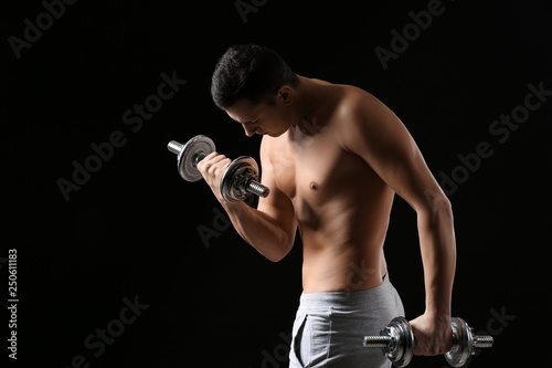 Sporty young man training with dumbbells against dark background