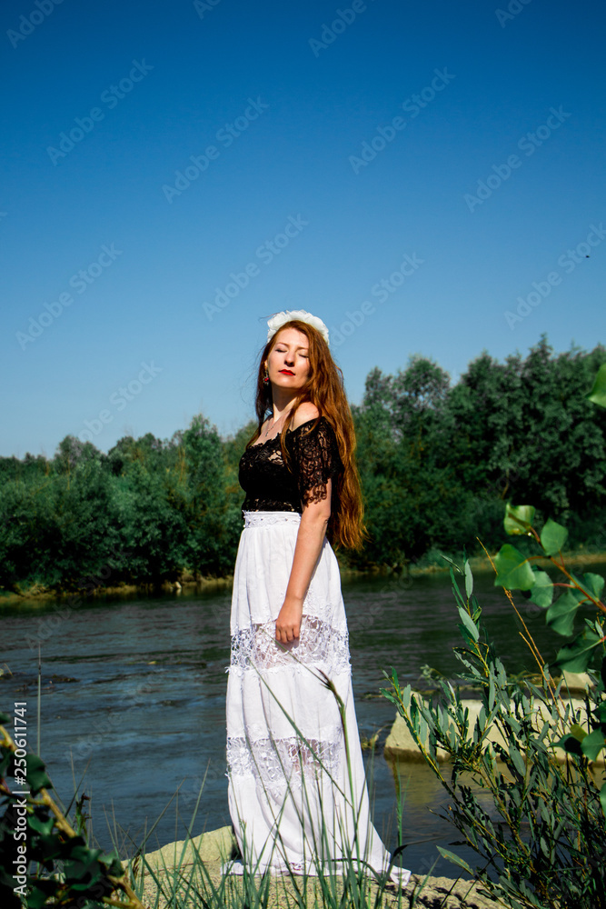 Young redhead woman in dress on the rock around the water and green leaf Young redhead woman in dress on the rock around the water and green leaf