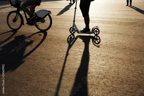 silhouette kick scooter, silhouette of a man and a bicycle wheel with backlight. Long contrasting shadows on the asphalt. Contre-jour at sunset on a sunny street in summer photo