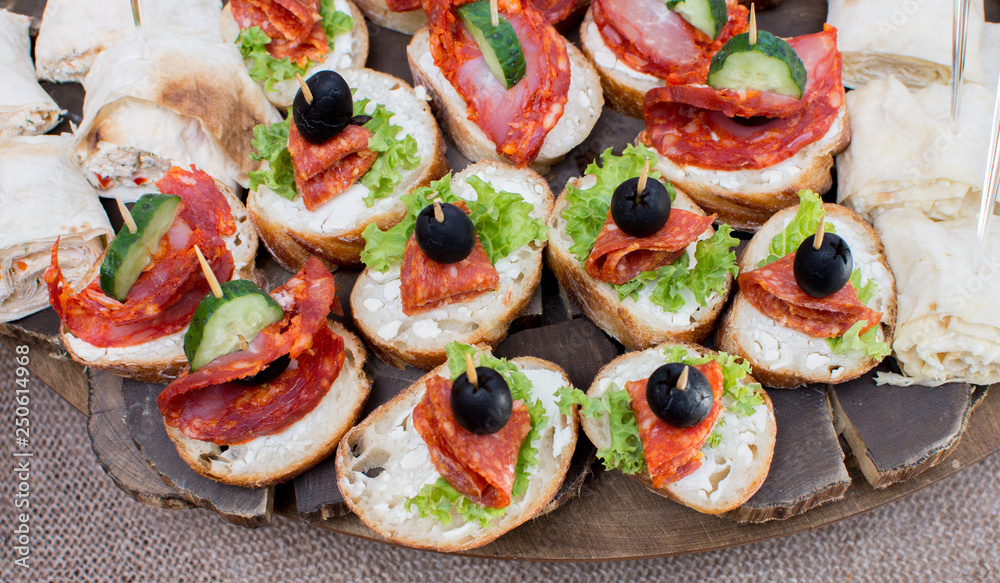 Sandwiches with salami and olives on a wooden plate