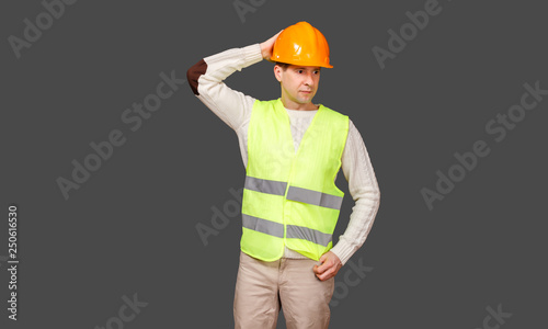 The man the builder in a helmet and a vest scratches a nape