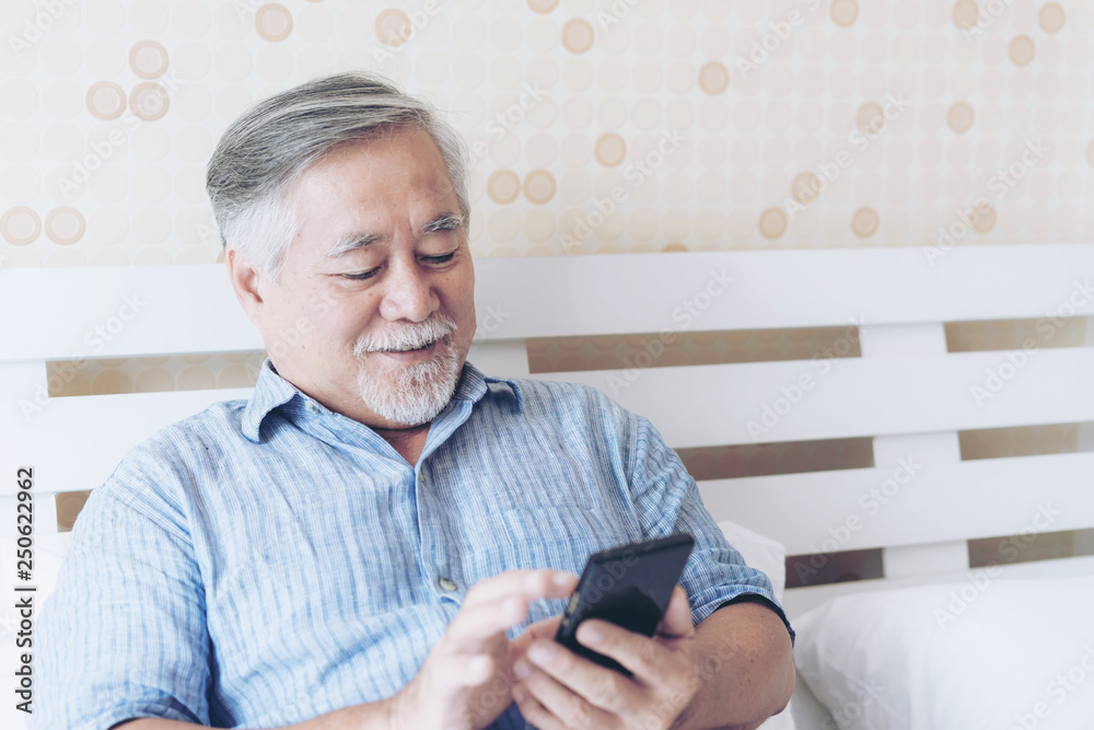 Senior Male using a smartphone , smiling feel happy in bed at home - lifestyle senior concept Senior Male using a smartphone , smiling feel happy in bed at home - lifestyle senior concept