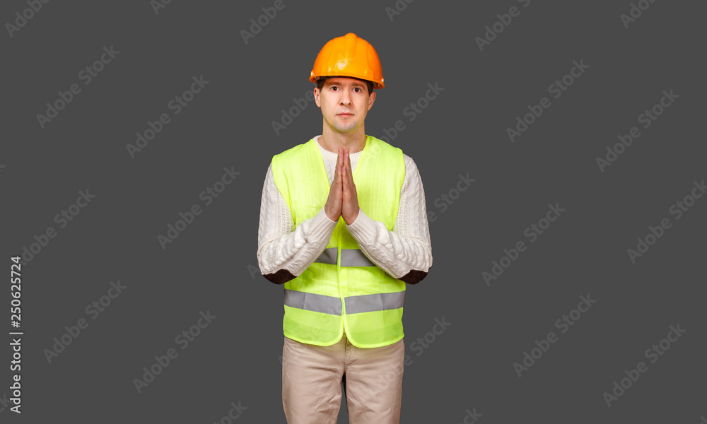 The man the builder in a helmet and a vest put palms together in a prayer The man the builder in a helmet and a vest put palms together in a prayer