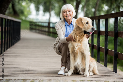 Фотография happy senior woman with golden retriever dog on wooden bridge