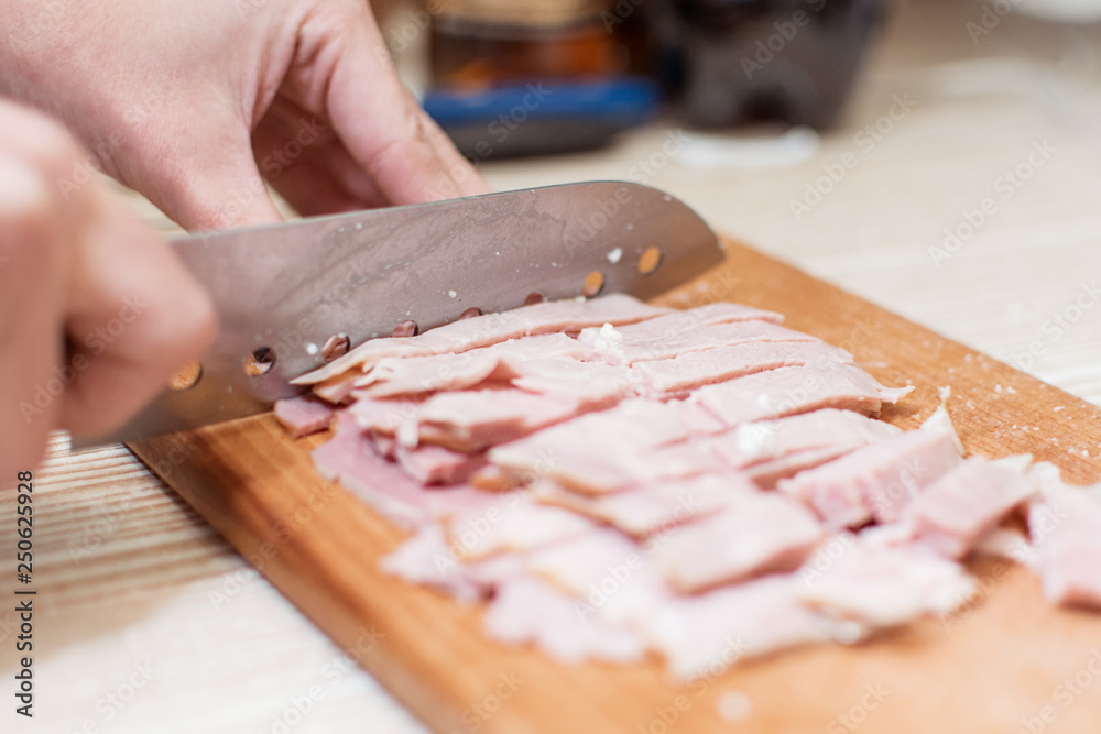 Woman cuts sausage, ham on a cutting board.