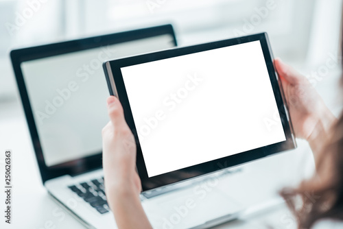 Close-up of woman holding digital tablet while sitting at table with laptop.