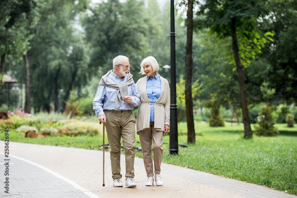 happy senior couple talking while walking in park happy senior couple talking while walking in park