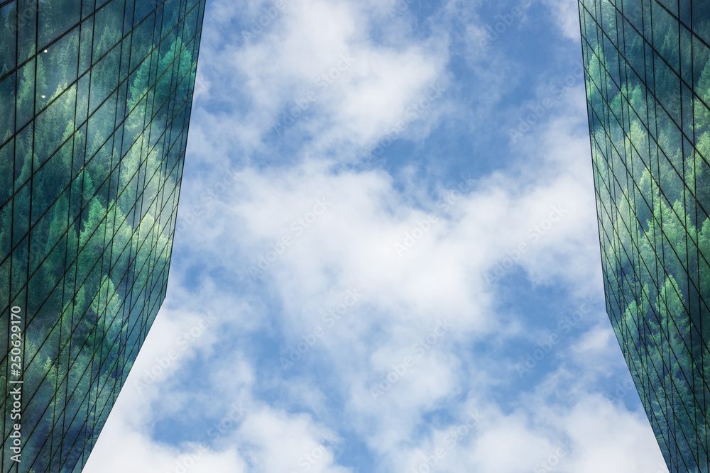 Modern building with forest reflected in windows and facade,blue sky and clouds in background. Sustainable, green energy city, low-energy, environmental concept.