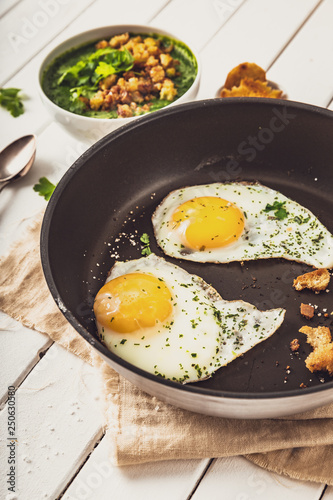 two fried eggs in a pan with herbs and salt for spinach