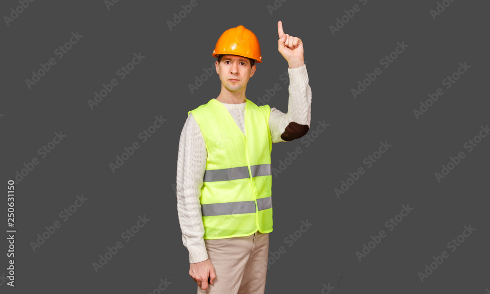 The man the builder in a helmet and a vest points a finger up