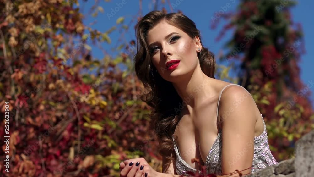 A luxurious young girl in an evening dress is leaning on the railing of an old stone balcony on which grows wild grapes with red and yellow leaves. A luxurious young girl in an evening dress is leaning on the railing of an old stone balcony on which grows wild grapes with red and yellow leaves.