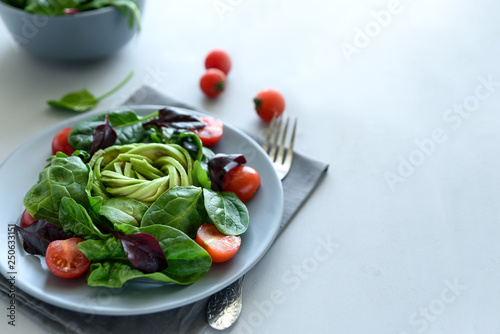 Salad mix with avocado, spinach, tomatoes and beet leaves on gray wooden background. Vegetarian food concept. Selective focus.
