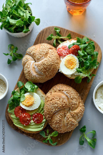 Bagel sandwiches with cream cheese, avocado, tomatoes, egg and greens on gray wooden background. Selective focus. Healthy eating or vegetarian food concept