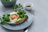 Toast (sandwich) with cream cheese, avocado, fried egg and greens on gray wooden background. Selective focus. Healthy eating or vegetarian food concept