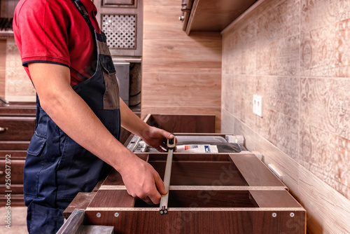 A young worker is assembling modern wooden kitchen furniture.