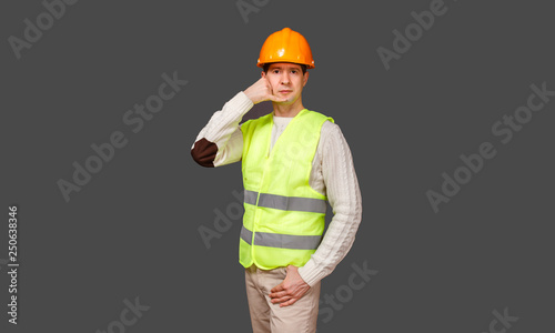 The man the builder keeps fingers of hands about an ear in a helmet and a vest and a mouth of the head