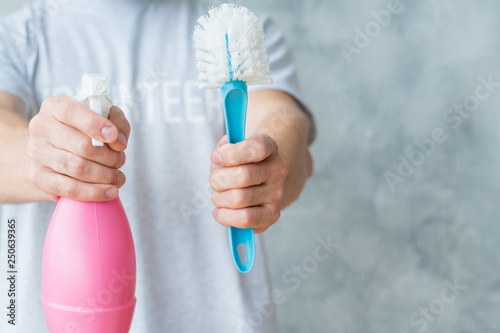 Housekeeping concept. Man holding atomizer and brush. Copy space on grey background.