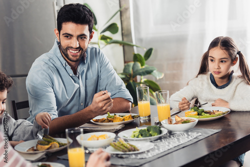 handsome latin father looking at wife while having lunch near daughter and son
