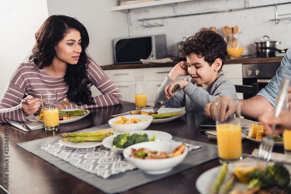 selective focus of latin woman looking at cute son having lunch near father and daughter at home selective focus of latin woman looking at cute son having lunch near father and daughter at home