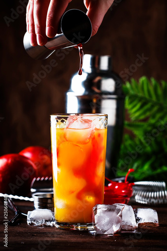 Summer tequila sunrise cocktail with silver tequila, grenadine syrup, orange and ice cubes. Wooden bar counter in the beach bar. Bartender preparing cocktail. Selective focus. Place for text photo