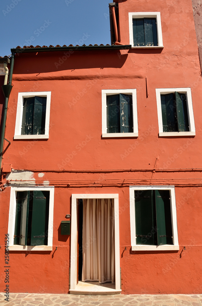 Mediterranean style. Windows with green shutters on orange wall. Colourful painted windows. Burano island near Venice, Italy. Abstract background, texture
