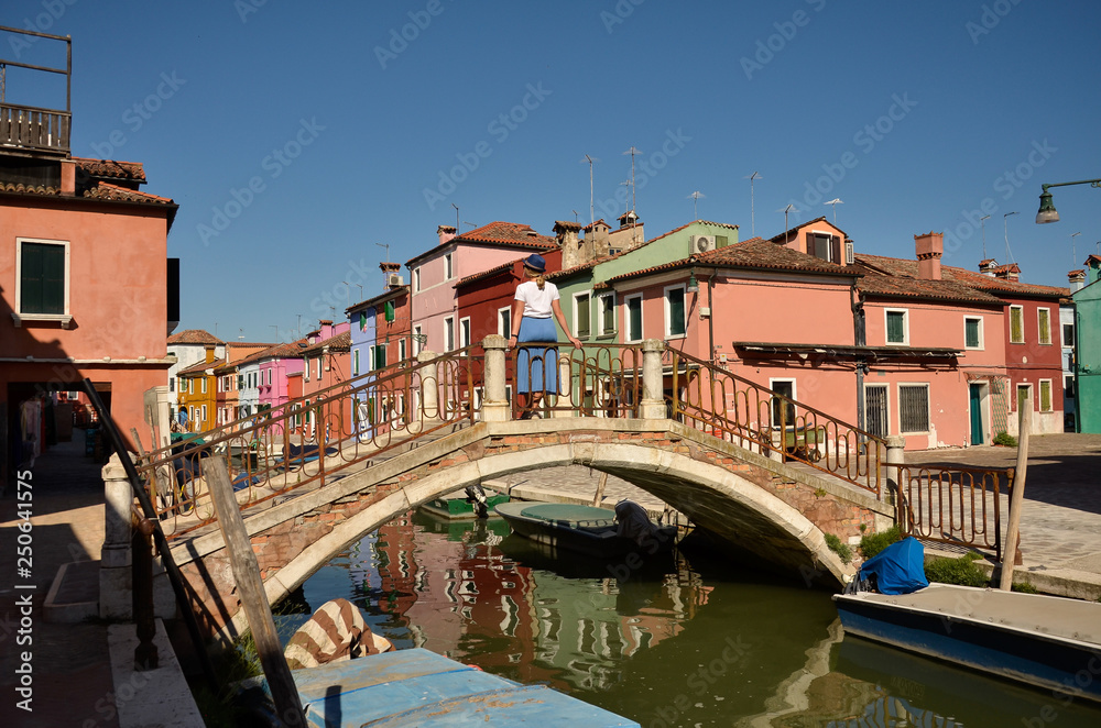 Scenic canal with colorful buildings in Burano island, Venice, Italy. Woman tourist