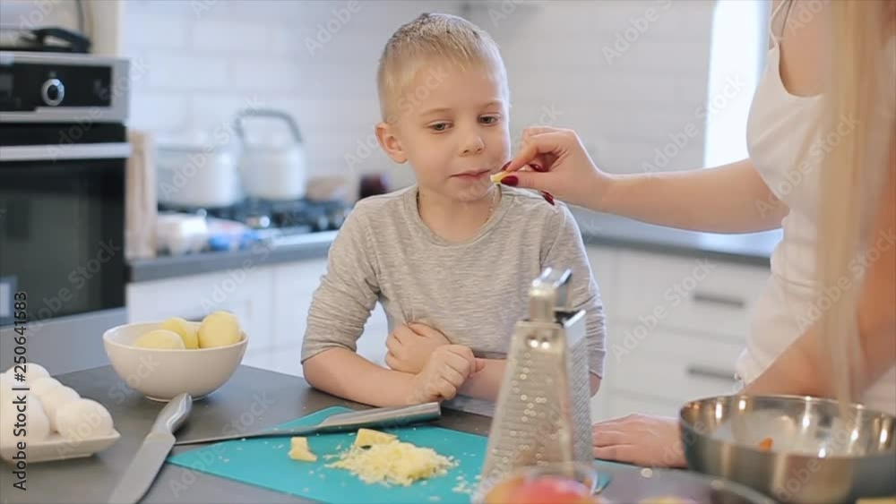 Mommy giving chopped cheese to her son on the kitchen. Young mother and cute beautiful son with big eyes cooking toghether. Family making pizza. Mommy giving chopped cheese to her son on the kitchen. Young mother and cute beautiful son with big eyes cooking toghether. Family making pizza.