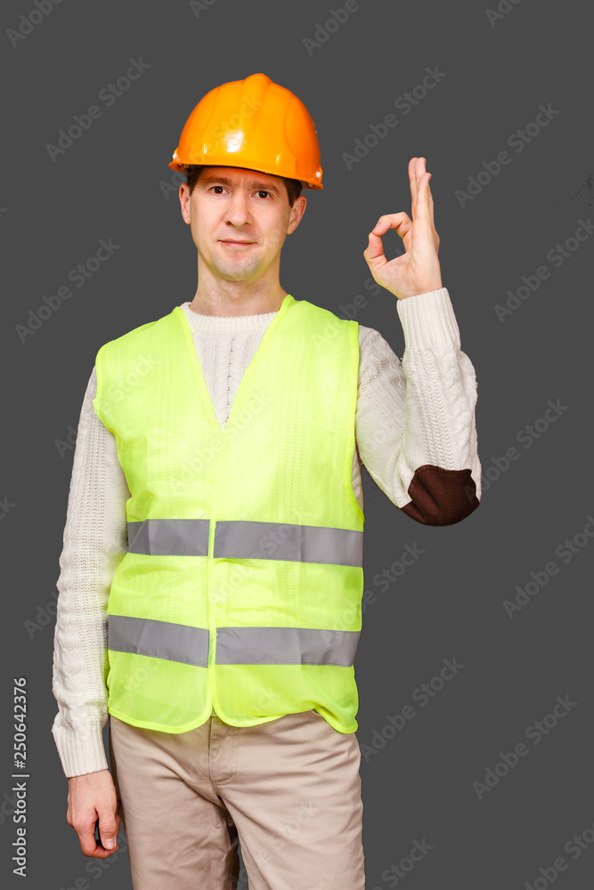 The man the builder in a helmet and a vest, gesture - OK, everything is good