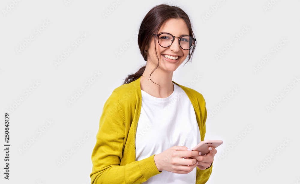 European beautiful brunette smiling young woman using cellphone, messaging to her friend. Happy female chatting with her boyfriend via smart phone, looking at the camera. People, technology, emotion European beautiful brunette smiling young woman using cellphone, messaging to her friend. Happy female chatting with her boyfriend via smart phone, looking at the camera. People, technology, emotion