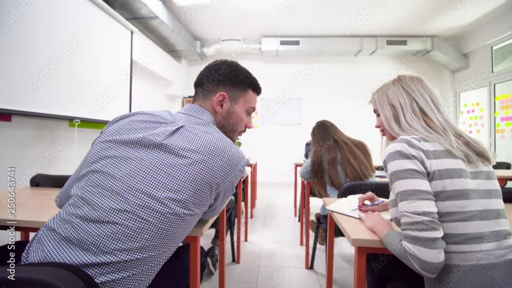 blond female student asking for advice from a fellow colleague in classroom during a test blond female student asking for advice from a fellow colleague in classroom during a test