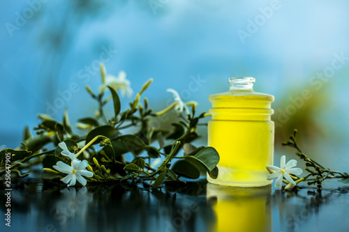 Close up shot of extracted essential oil of Indian jasmine flower in a transparent glass bottle on wooden surface with raw jasmine flowers. photo