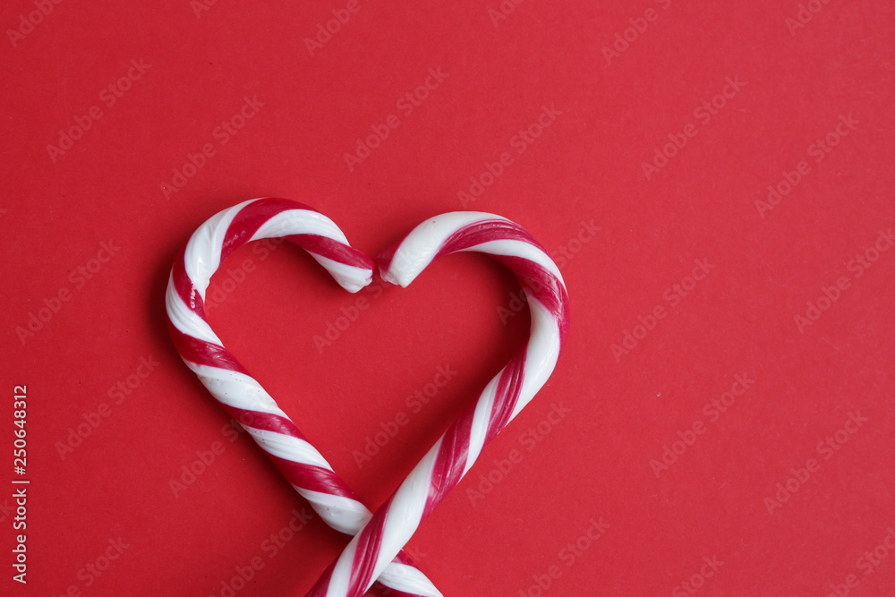 Sweet traditional Christmas candy isolated on red background. Two candy canes making a heart on a red background, Candy cane heart. Copyplace, space for text and logo. Sweet traditional Christmas candy isolated on red background. Two candy canes making a heart on a red background, Candy cane heart. Copyplace, space for text and logo.