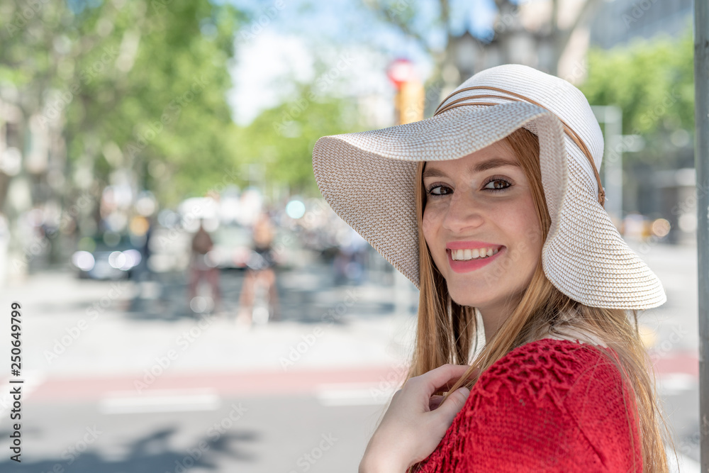 Happy girl with straw hat smiling visiting city