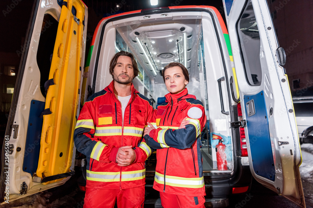 Paramedics in red uniform standing in front of ambulance car Paramedics in red uniform standing in front of ambulance car