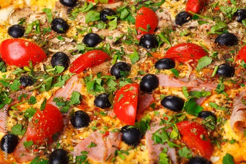 Close up Italian pizza with melted cheese, red cherry tomatoes, black olives, ham, and green leaves on a brown table decorated with mushrooms, red hot chili pepper and cherry tomatoes
