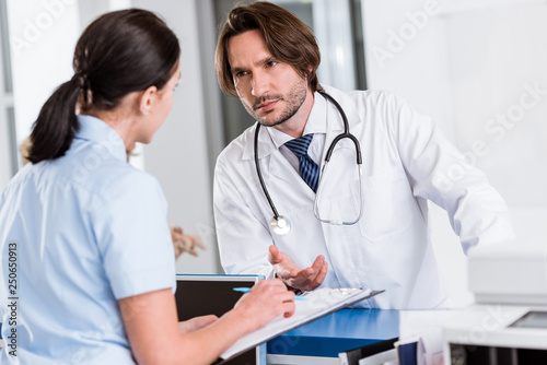 Serious doctor with stethoscope talking to nurse in clinic