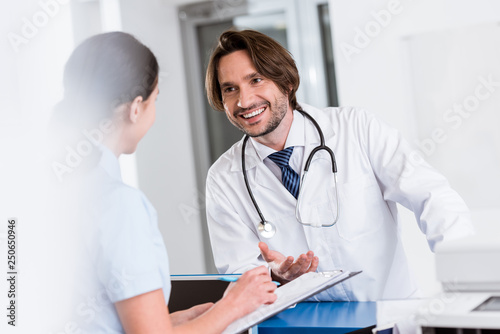 Smiling doctor with stethoscope talking to nurse