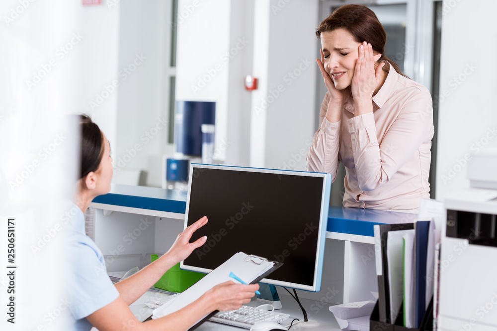 Worried patient talking to nurse and touching head with closed eyes Worried patient talking to nurse and touching head with closed eyes