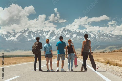 Vászonkép Friends group travellers stands on straight road against mountains