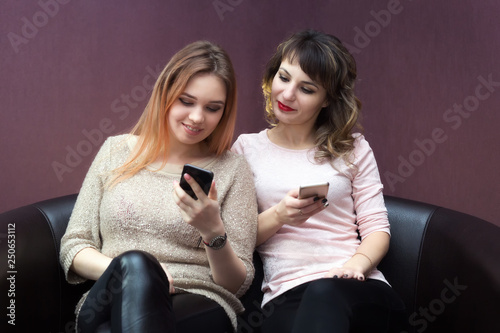 Close friends sit on the couch talking to each other and on the Internet.